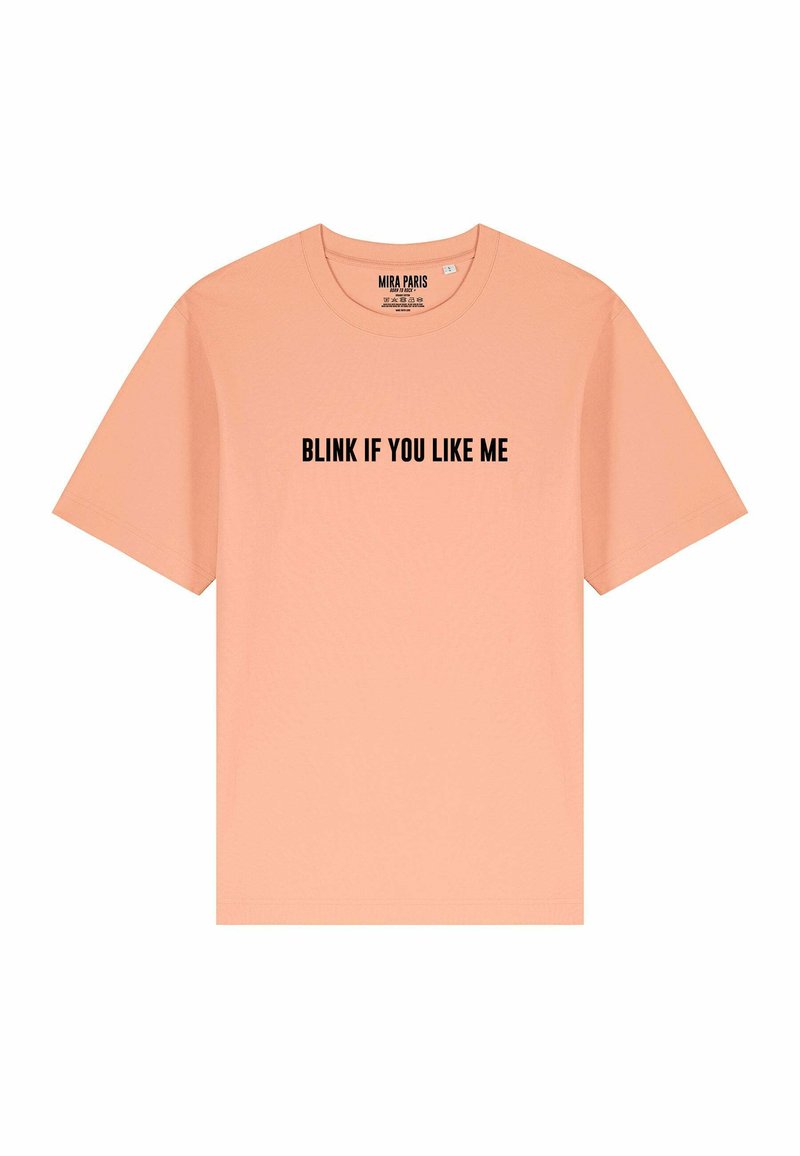 Perzikkleurig katoenen T-shirt met korte mouwen en een ronde hals. De voorkant heeft vetgedrukte zwarte tekst: "KNIPPER ALS JE MIJ LEUK VINDT."