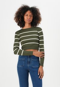Kaki ribbet cropped genser med hvite horisontale striper, lange ermer. Brukt med høyt liv blå denim jeans med to baklommer.