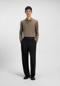 Polo a maniche lunghe in marrone smorzato, con colletto e tre bottoni, abbinata a pantaloni neri a vita alta e scarpe nere.