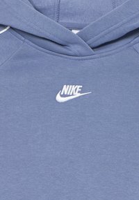 Zils kokvilnas kapuce, kas aprīkota ar auklu regulējamu kapuci, ribotām aprocēm un baltu izšūtu Nike logo uz krūtīm. Gluda tekstūra, ikdienišķs dizains.