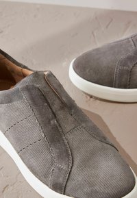 Gray suede slip-on shoes with elastic side panels, white rubber soles, and visible stitching details on the upper material.