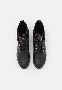 Botines negros de cuero liso con punta redondeada, ojales plateados y un acento de tachuelas en el cuello, con cremalleras laterales.