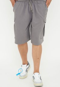 Grå cargoshorts med elastiskt midjeband och dragsko, med sidofickor. Matchas med vita sneakers med grå accenter.