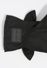 Tela negra con acabado texturizado, presenta un diseño fruncido y un parche rectangular con el logo en relieve.