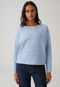 Maglione pullover a righe blu e bianche con scollo ampio e maniche lunghe, caratterizzato da una texture a coste e una vestibilità rilassata. Indossato con jeans scuri.