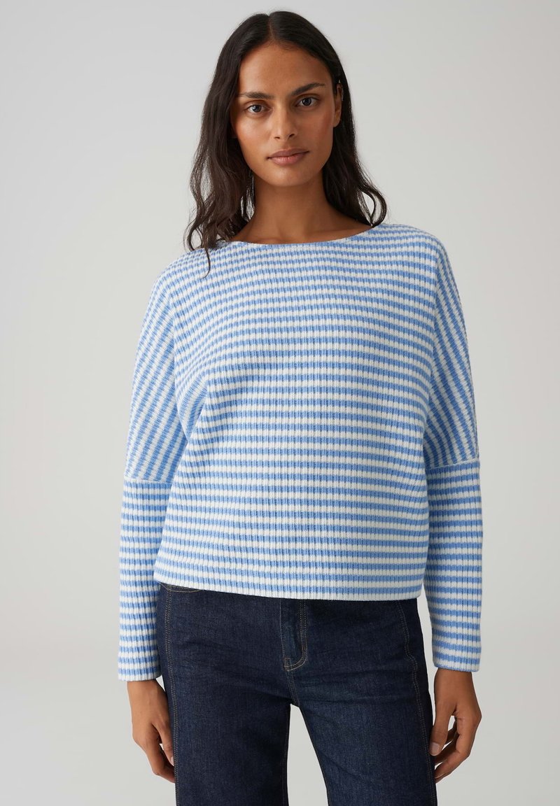 Maglione pullover a righe blu e bianche con scollo ampio e maniche lunghe, caratterizzato da una texture a coste e una vestibilità rilassata. Indossato con jeans scuri.