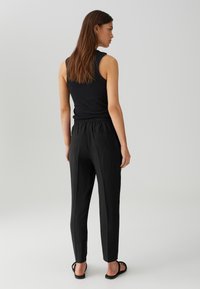 Haut sans manches noir et pantalon noir fuselé avec taille élastique et poches arrière, vu de dos, texture plate, design décontracté.
