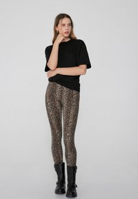 Czarna, przejrzysta koszulka, legginsy w panterkę i czarne botki za kostkę. Legginsy mają teksturowany wzór. Prosty, casualowy look z warstwami.