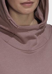 Sweat à capuche en tissu mauve clair, présentant une texture douce, un cordon de serrage réglable et un col rond avec une coupe décontractée.
