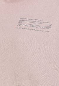 Der pinke Baumwollstoff zeichnet sich durch bedruckten Text aus, der Selbstpflege und Glück fördert, und hat eine glatte Textur sowie ein schlichtes Design.