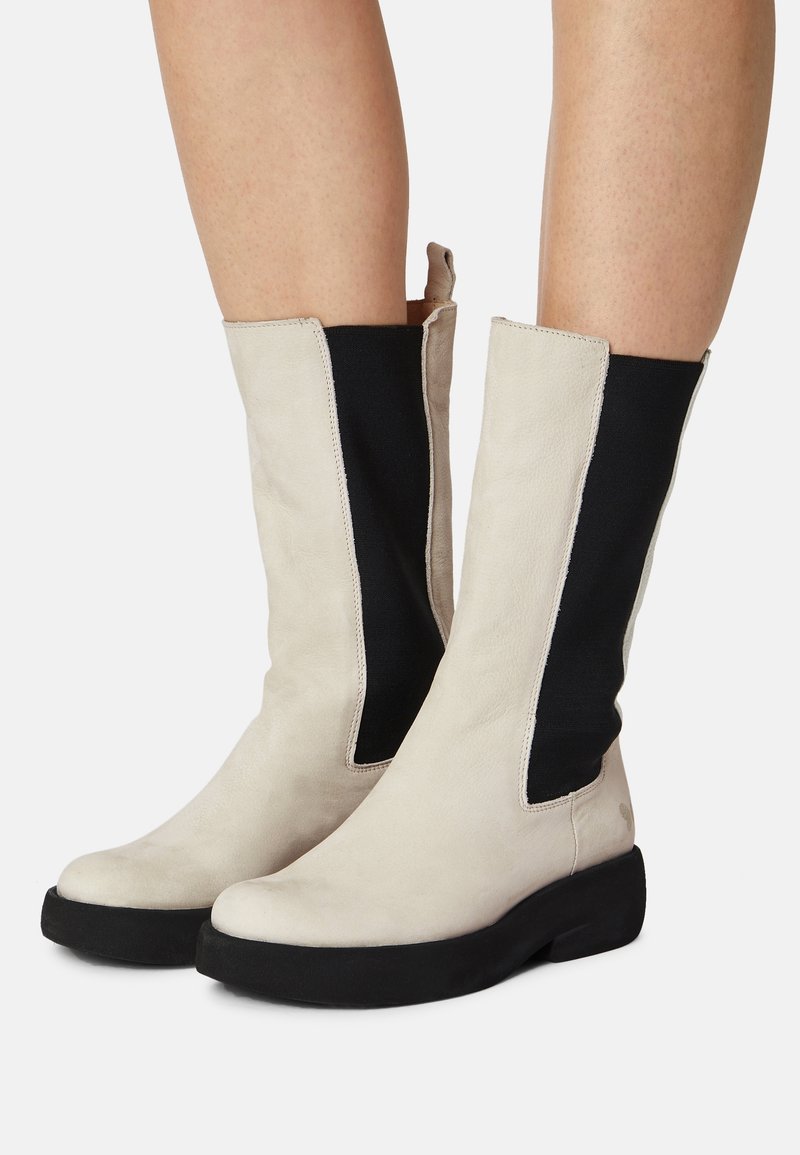 Kozaki do kolan z miękkiej off-white skóry z czarnymi elastycznymi panelami po bokach, okrągłym noskiem i grubą czarną podeszwą. Minimalistyczny design.