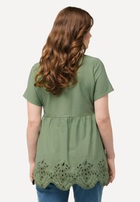 Blusa verde claro con mangas cortas, cintura fruncida y dobladillo bordado con forma de concha. Tejido suave con un patrón floral texturizado en la parte inferior.