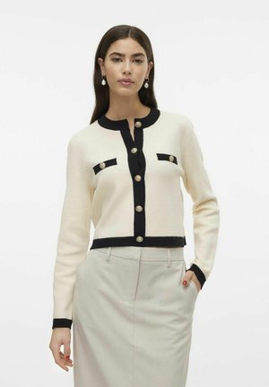 White cardigan with black trim, round neck, and gold buttons. Features two chest pockets outlined in black. Soft texture, cropped design.