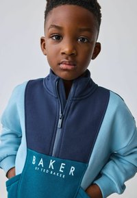 Sudadera con cremallera en azul y marino con un diseño en bloques de color, alta cuello y logo frontal "BAKER by TED BAKER." Tejido suave y puños acanalados.