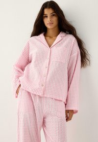 Różowy i biały zestaw piżamowy w kratkę wykonany z lekkiego materiału. Zawiera koszulę na guziki i luźne spodnie z elastycznym pasem.