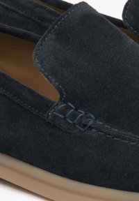 Tmavě modré semišové mokasíny s prořezávaným vzorem, zdobené kontrastním světle modrým prošíváním a hladkou světlou gumovou podrážkou.