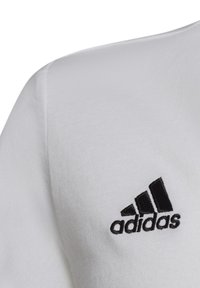 Weißes Baumwoll-T-Shirt mit weicher Textur, das ein schwarzes gesticktes Adidas-Logo auf der oberen linken Seite zeigt.