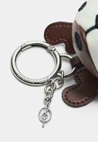 Portachiavi in pelle marrone con un anello circolare in metallo argentato, un charm a forma di nota musicale e componenti decorativi in tessuto.