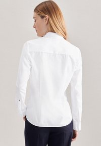 Camicia bianca a maniche lunghe con colletto a punta, dettaglio sulla spalla posteriore e polsini con bottoni. Tessuto liscio e vestibilità sartoriale.