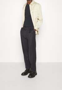 Beige knappad skjorta, marinblå t-shirt, marinblå plisserade byxor och svarta snörskor. Ren design med släta texturer, inga synliga mönster.