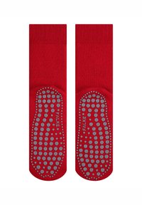 Calcetines de algodón rojos con puntos de goma gris texturizados y antideslizantes en las suelas. Presentan un puño acanalado para un ajuste seguro. Nombre de la marca "FALKE" visible.