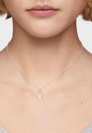 Collana in catena d'argento con un piccolo ciondolo ovale raffigurante la silhouette di un orso indossata intorno al collo di una persona su uno sfondo semplice.