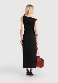 Gaun hitam yang pas di badan dengan satu lengan dan resleting di belakang. Model memegang tas tot suede berwarna karat dan memakai sepatu hak tinggi hitam.