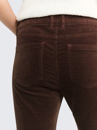 Pantalones de pana marrones con un diseño ajustado, dos bolsillos traseros y costuras visibles. La textura es suave y esponjosa.