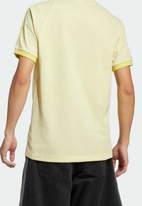 Gul bomulls t-shirt med kort ärm och kontrasterande ljusgula muddar. Baksidan har en enkel, slät yta utan mönster.