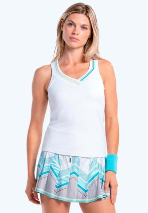 Blonde Frau trägt ein weißes ärmelloses Oberteil, einen blau gemusterten plissierten Rock und ein blaues Armband, steht vor einem weißen Hintergrund.