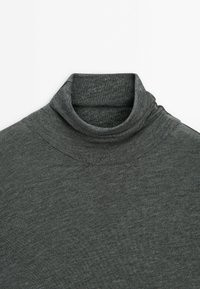 Pull à col roulé gris foncé plié en tissu tricot fin sur fond blanc.