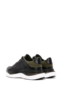 Sneakers in pelle nera con dettagli verde oliva, caratterizzati da una tomaia texture, forma arrotondata e suola bianca imbottita.