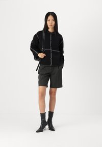 Zwarte gestructureerde trui met witte stikipdetails, grijze op maat gemaakte shorts en kniehoge zwarte haklaarzen; minimalistisch ontwerp met een moderne silhouet.
