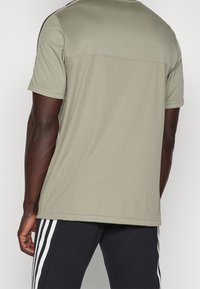 Olivgrön kortärmad sporttröja med vertikala ränder, enfärgad bak, rund halsringning och svarta sidodetaljer. Texturerat tyg.