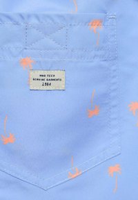 Svetlomodrá tkanina s malými oranžovými vzormi paliem. Obsahuje štítok s nápisom "HMG TEEN GENUINE GARMENTS 1984" na vyšitom nápletu.