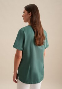 Top a maniche corte in tessuto verde tenue, caratterizzato da un collo tondo, vestibilità ampia e spacchi laterali, completato da una texture liscia e linee pulite.