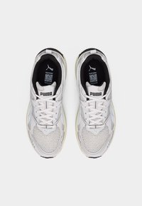 Λευκά αθλητικά παπούτσια Puma με λεπτομέρειες από δίχτυ και κορδόνια, φωτογραφημένα από ψηλά, που δείχνουν το μαύρο εσωτερικό και την ετικέτα με το λογότυπο στη γλώσσα.