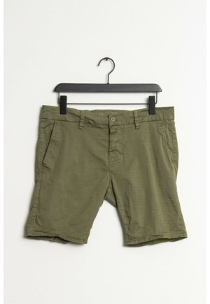 Grøn mønstret herreshorts hængende på en sort bøjle mod en hvid baggrund.