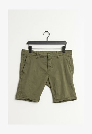 Shorts pour hommes à motif vert suspendus sur un cintre noir sur un fond blanc.