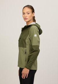 Groene, lichte jas met capuchon, met contrasterende tinten, ritszakken en een klein logo op de linkermouw.