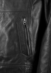 Zwarte leren jas met een close-up van een ritszak met een textuurpaneel, een gladde afwerking en zichtbare stikdetails.