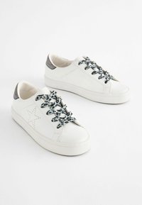 Białe skórzane sneakersy z perforowanym wzorem gwiazdy, sznurowadłami w leopardzim wzorze i metaliczno-szarymi akcentami na pięcie. Płaska podeszwa platformowa.
