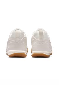 Sapatos atléticos brancos com um cabedal sintético liso, painéis de malha respirável e sola de borracha de gengibre. Inclui uma alça de tecido na parte de trás.