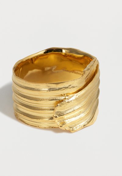 Ευρύ χρυσό δαχτυλίδι με υφασμένες, στρωματοποιημένες λωρίδες και ακανόνιστη, κυματιστή λεπτομέρεια άκρου σε λευκό φόντο.
