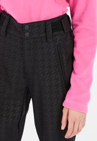 Pantalons de neige noirs avec motif pied-de-poule, comportant une poche zippée, deux boutons à la taille et une sangle de réglage en Velcro.