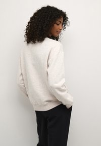 Hellbeige Sweatshirt mit lässiger Passform, gerippten Bündchen und Saum, strukturiertem Stoff und Rundhalsausschnitt, kombiniert mit schwarzen Hosen.