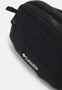 Bolsa Columbia preta com material em fleece suave e texturizado, uma seção em tecido liso e fecho com zip. Inclui um patch com o logo.
