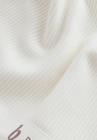 Witte geribde stof met een zachte textuur en subtiele glans, met een label met "6" in een gedempte lavendelkleur.