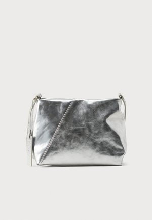 Sac bandoulière en cuir métallisé argenté avec un détail de couture diagonale et une fine sangle réglable sur un fond uni.