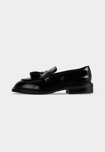Μαύρο δερμάτινο loafer με φούντες, χαμηλό στρωμένο τακούνι και στρογγυλεμένο δάκτυλο, εμφανίζεται σε πλαϊνό προφίλ σε λευκό φόντο.